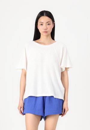 Hvit oversized t-skjorte med korte ermer, lett stoff og rund hals, kombinert med blå teksturerte shorts.