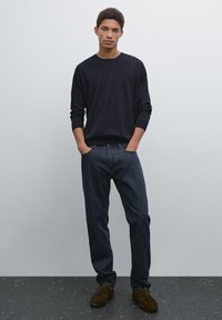 Dark blue knit sweater, relaxed fit dark jeans, and brown lace-up shoes. Smooth fabric with ribbed cuffs, simple design. Plain background.
