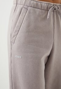 Grå joggebukser laget av teksturert stoff, med sidelommer, elastisk midje med snor og en liten logoetikett.