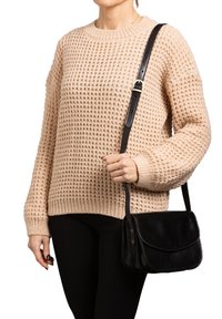 Maglione beige lavorato a maglia con un motivo testurizzato, abbinato a una borsa a tracolla in pelle nera, con tracolla e chiusura a pattina.