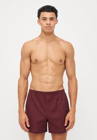 Bordeaux badeshorts med elastisk midjebånd, knappdetalj og en avslappet passform, laget av lett stoff.
