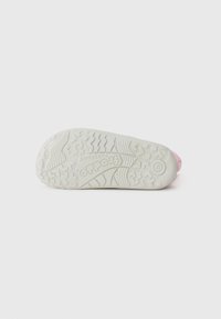 Witte schoenzool met gestructureerde grippatronen. Merken zichtbaar, met een roze accent op de hiel, ontworpen voor comfort en grip.