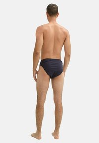 Dunkelblaue Schwimmshorts aus strukturiertem Material, mit einem mittelhohen Bund und moderater Bedeckung, von hinten gezeigt.