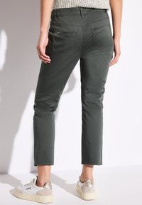 Dunkelgrüne, kn�öchellange Hose mit schlanker Passform, ausgestattet mit Gesäßtaschen und einem Reißverschlussdetail. Tragen Sie sie mit weißen Sneakers und einem Strickoberteil.