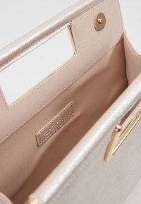 Metallinhohtoinen beige käsilaukku, jossa on teksturoidtu pinta, kullanvärinen läppäkiinnitys ja pehmeä beige sisusta, merkitty "Forever New" -brändillä.