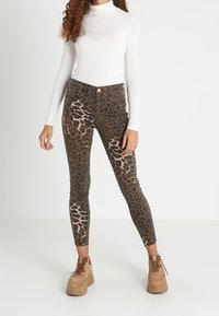 Jeans skinny de estampado de leopardo en marrón y negro, con cintura alta, corte ajustado y bolsillos frontales. Combinados con una blusa blanca de manga larga.