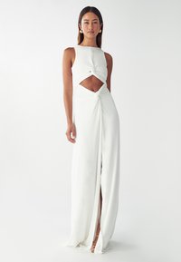 Vestido maxi blanco con diseño sin mangas, detalle de nudo en el frente y una abertura alta en el muslo, confeccionado en una tela suave y fluida.