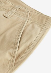 Pantaloni scurți din bumbac bej, cu față netedă, buzunarelaterale și cusături întărite la talie. Textură fină și detalii de design casual vizibile.