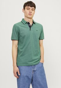 Grøn kortærmet polo T-shirt med en marineblå krave detail, med en subtil struktur og logo på venstre bryst, parret med blå jeans.