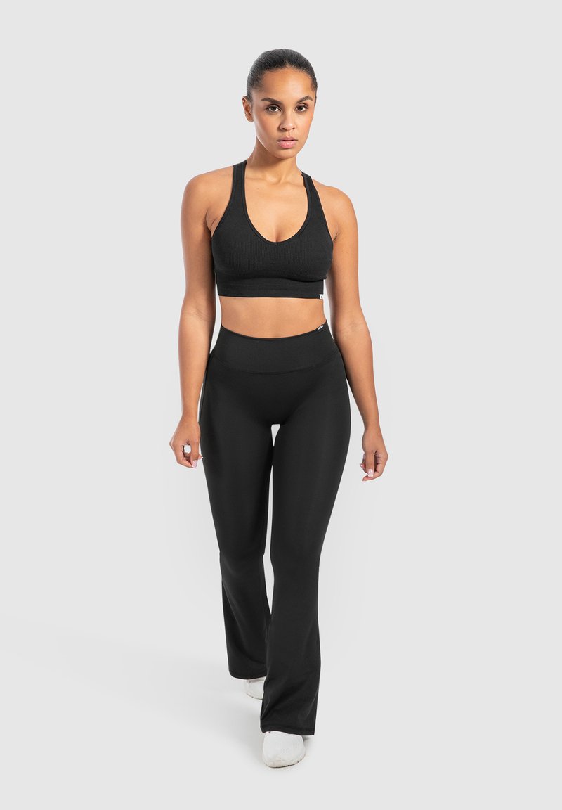 Top sportivo nero a coste abbinato a leggings neri a vita alta e lisci. Entrambi presentano un design aderente adatto per abbigliamento sportivo.