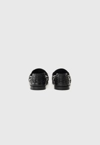 Schwarze Slipper aus Leder mit geflochtenem Design, ausgestattet mit einer flachen Sohle und offenem Rücken für ein einfaches An- und Ausziehen.