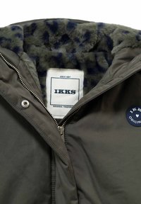 Groene jas met leopardenprint faux fur voering, gedeeltelijk open geritst en toont het IKKS merkimlabel en een ronde patch op de borst.