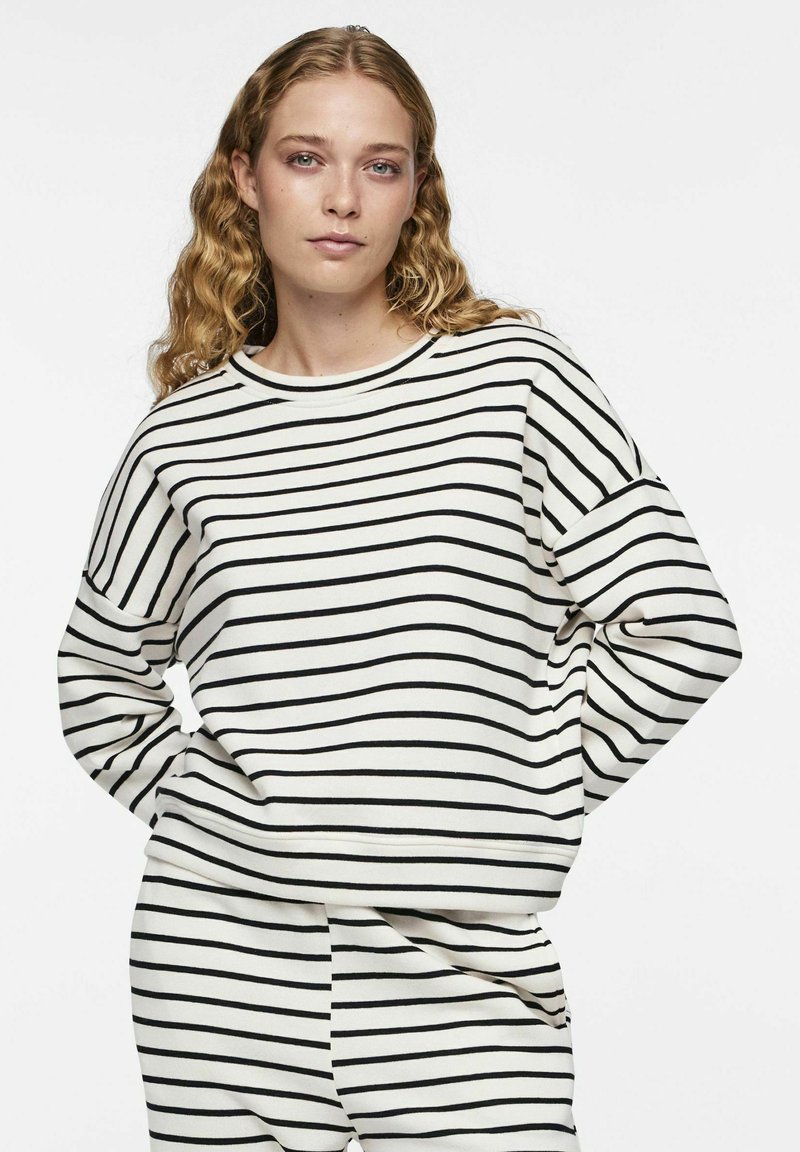 Sweatshirt rayé en crème avec des lignes horizontales noires, doté d'un col rond et d'une coupe décontractée, fabriqué en mélange de coton doux.