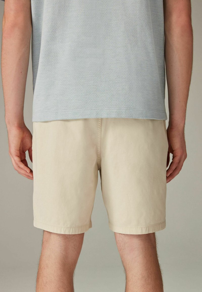 Shorts en coton beige avec une coupe droite et un ourlet cousu, associés à un t-shirt texturé gris clair. Design minimaliste.