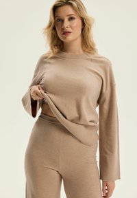 Beżowy sweter z dzianiny z długimi rękawami i okrągłym dekoltem, w połączeniu z pasującymi spodniami o wysokim stanie, o gładkiej fakturze.