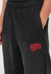 Svarte joggebukser med elastisk midje og sidelommer. Har brodert rød "Billionaire Boys Club"-logo på venstre lår.