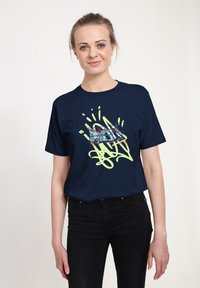 Námořnická modrá bavlněná trička s grafickým designem v zelené barvě, obsahující kulaté tvary a stylizovanou ilustraci vozidla.