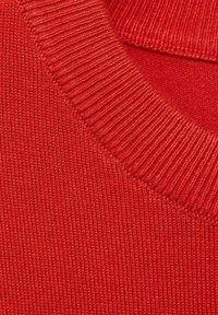 Röd stickad tröja med ribbad halsringning och slät textur. Närbild som framhäver stickmönstret och den rika färgen.