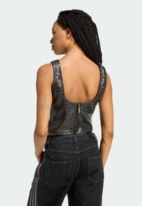 Czarny krótki top z tłoczeniem na wzór krokodyla, z niskim dekoltem na plecach i zapięciem na zamek. W zestawie z czarnymi, wysokim stanem jeansami z bocznymi paskami.