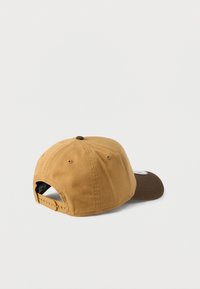 Καφέ και μπεζ καπέλο του μπέιζμπολ με κυρτή γείσο, υφασμάτινο ρυθμιζόμενο λουράκι και κεντημένο λογότυπο στο πίσω μέρος, με υφή υφάσματος.