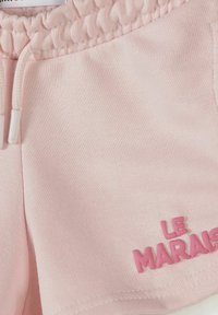Tissu rose clair avec taille élastique et cordon de serrage, arborant un texte en relief rose "LE MARAIS" près de l'ourlet.