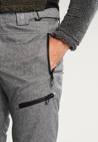 Pantalons gris texturés avec plusieurs poches zippées. Dotés d'une taille lisse et de zips noirs pour des accents fonctionnels.