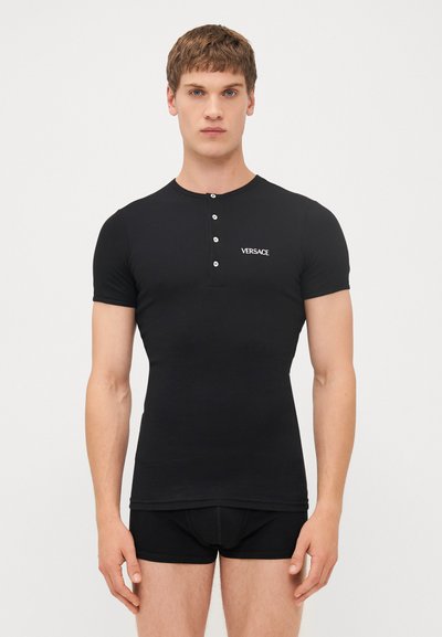 Black short-sleeve henley shirt made of a smooth fabric with five white buttons at the collar, featuring a small Versace logo on the chest.
