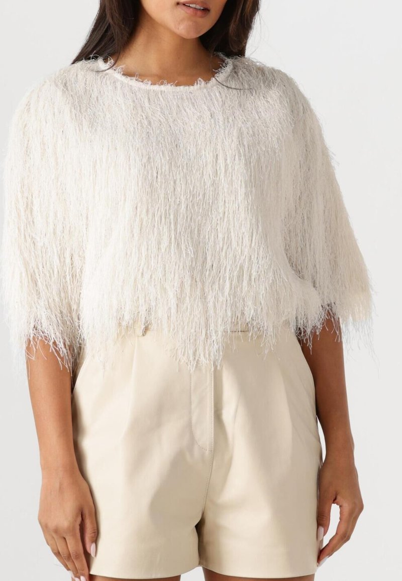 Λευκή υφασμάτινη μπλούζα με βολάν, κοντά μανίκια και στρογγυλή λαιμόκοψη, συνδυασμένη με μπεζ προσαρμοσμένες βερμούδες.