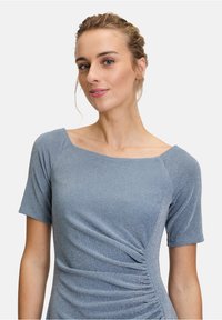 Blå metallikklänning med korta ärmar, fyrkantig halsringning, sidopuffdetalj och en slät textur. Tyget har en subtil glans.