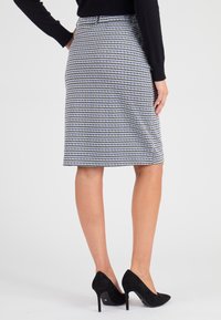 Houndstooth-kokerrok in zwart-wit, kniehoogte met een gladde textuur, gecombineerd met zwarte suède hoge hakken.