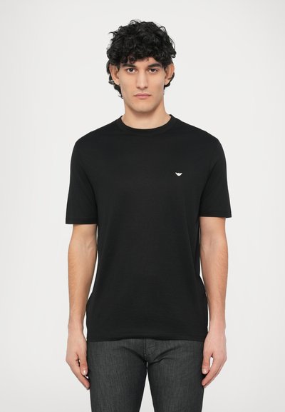 Schwarzes Baumwoll-T-Shirt mit Rundhalsausschnitt, kurzen Ärmeln und einem kleinen Emblem auf der linken Brust. Weiche Textur, lässige Passform.