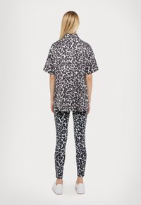 Camicetta a maniche corte con stampa leopardata e colletto alla coreana, abbinata a leggings coordinati. Entrambi i capi presentano una combinazione di colori bianco e nero.