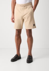 Beiga träningsshorts med elastisk midja och dragsko, med sidfickor och en liten svart logopatch på fållen.