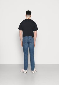 T-shirt preta de mangas curtas, jeans de ganga azuis e sapatilhas brancas com detalhes vermelhos. Apresenta bolsos traseiros planos e uma textura suave.