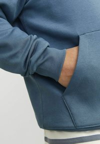 Blå sweatshirt med ribbede manchetter, der har en forlommes og en glat tekstur. Synlige sømdetaljer og en afslappet pasform.