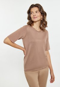 Lichtbruine top met korte mouwen en een ronde halslijn, gemaakt van zacht, gestructureerd materiaal; gecombineerd met beige broek.