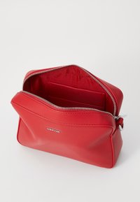 Rote Lederbeuteltasche mit Reißverschluss, ausgestattet mit einer glatten Textur und geprägtem Logo im Inneren. Fächer zur Organisation.