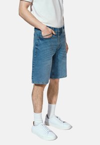 Szorty dżinsowe w jasnoniebieskim kolorze, prosty krój, podwinięte krawędzie oraz pięć kieszeni, połączone z białym t-shirtem i białymi trampkami.