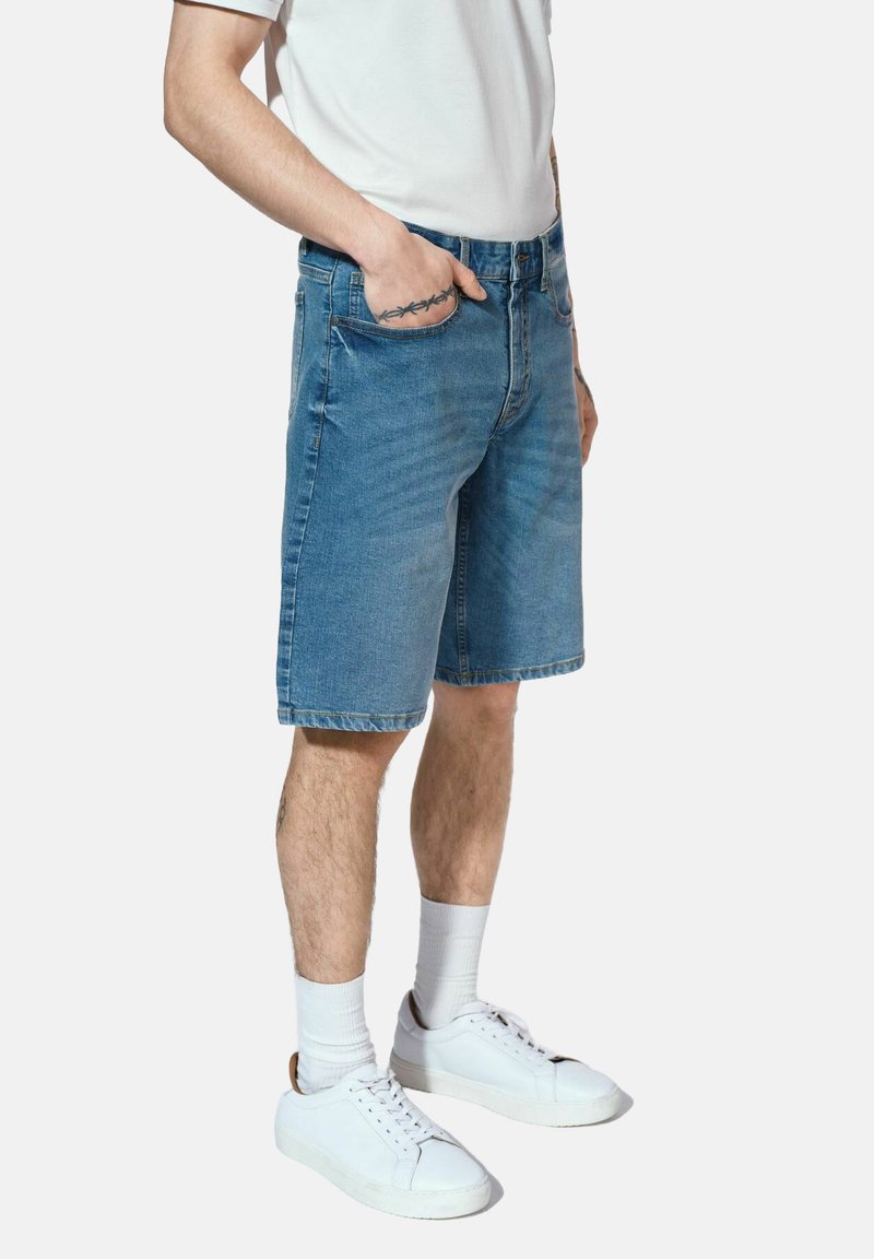 Szorty dżinsowe w jasnoniebieskim kolorze, prosty krój, podwinięte krawędzie oraz pięć kieszeni, połączone z białym t-shirtem i białymi trampkami.