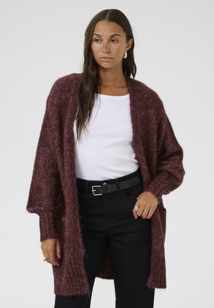 Burgundy knit cardigan with an open front, oversized sleeves, and a textured finish. Worn over a white shirt and black belt.