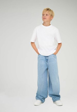 Hvit t-skjorte med korte ermer kombinert med løse lyseblå jeans. Antrekket har en avslappet passform og klassisk rund hals.