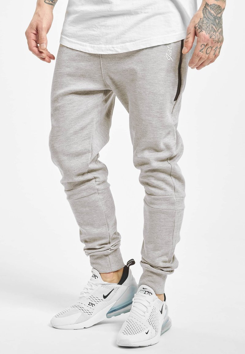 Light grey jogger pants made from soft fabric feature a tapered design, ribbed cuffs, and a black zippered pocket. Paired with white sneakers.