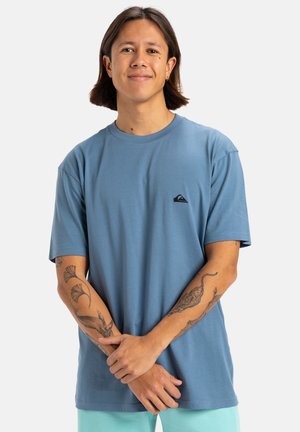 Camiseta de algodón de color azul claro con mangas cortas, cuello redondo y pequeño logo negro. La tela es suave y tiene un corte relajado.