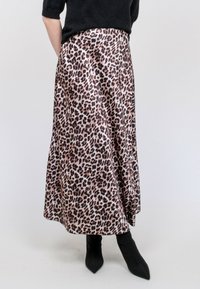 Jupe midi en imprimé léopard en tissu lisse, avec une coupe évasée, présentant des nuances de beige et de noir. Associée à des bottines noires ajustées.