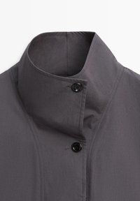 Kurtka o wysokim kołnierzu w ciemnoszarym kolorze z dwoma widocznymi czarnymi guzikami oraz detalami szwów na lekkiej tkaninie.