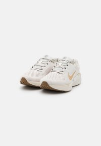 Pantofi sport albi cu un upper din plasă texturată respirabilă, accente gri deschis și o talpă din cauciuc cu modele de tracțiune maro.