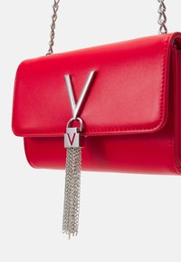 Borsa a mano in pelle rossa con finitura lucida, dotata di una fibbia argentata a forma di "V" e una nappina a catena attaccata a un'accoppiatura in metallo argentato.