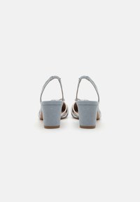 Lys blå hælsandaler med blokhæle, med en suede-overflade og justerbar ankelstrop. Åbent design med metalliske detaljer.