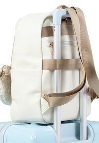 White textured backpack with beige straps secured on the handle of a light blue hard-shell suitcase.