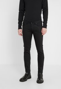 Černé slim-fit džíny s hladkou texturou, pětikapsovým designem, kovovým zapínáním a nenápadnými švy, doplněné o černé boty.